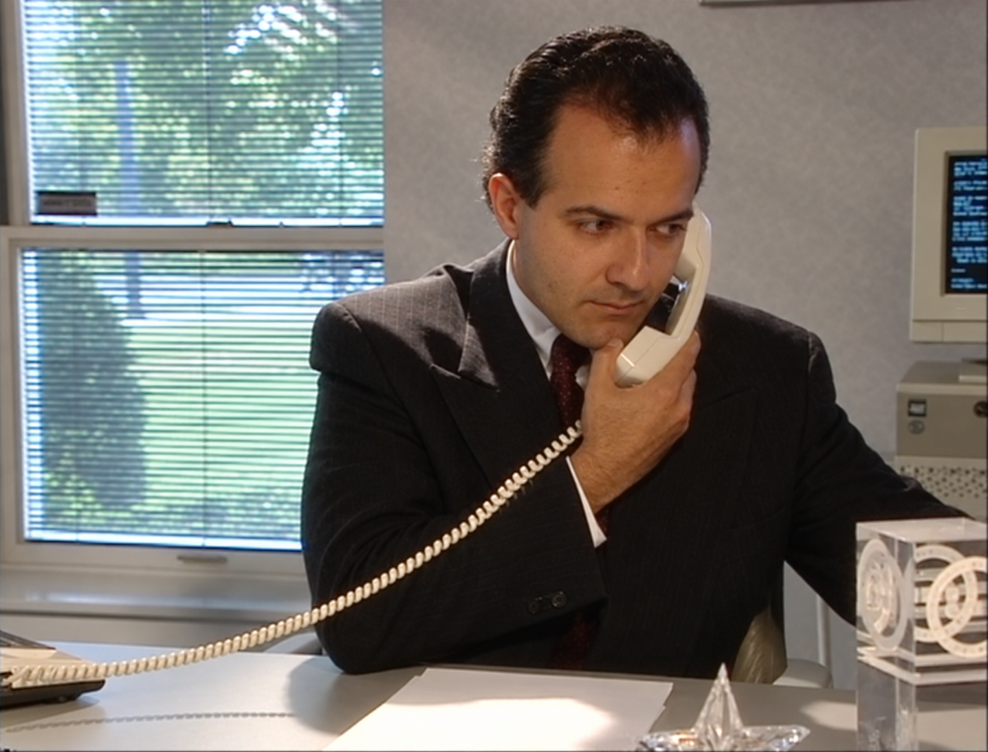AI-restored archival video still of a younger AJ Khubani at his office desk holding a white corded telephone
